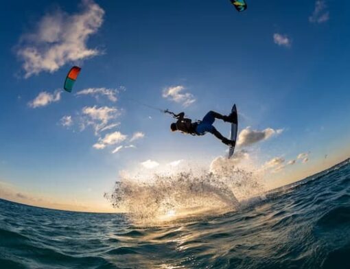 Esportista de Kitesurf na água, fazendo manobras no ar com o auxilio do kite durante um entardecer.