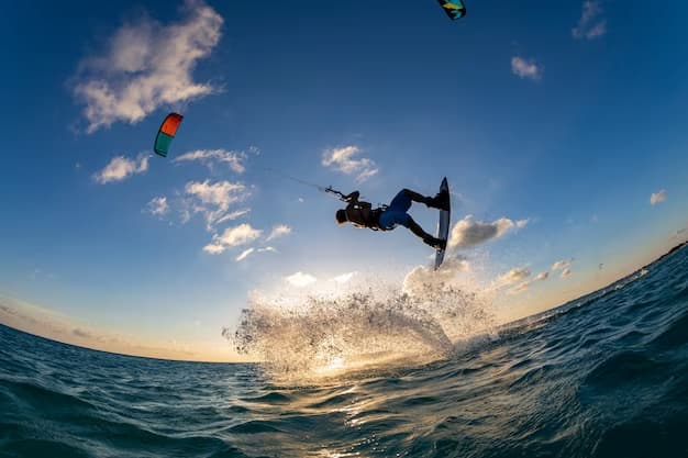 Esportista de Kitesurf na água, fazendo manobras no ar com o auxilio do kite durante um entardecer.