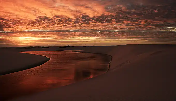 Visitantes caminhando entre lagoas de águas cristalinas e dunas nos Lençóis Maranhenses