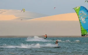 Kitesurfistas em águas rasas com duna ao fundo no litoral maranhense
