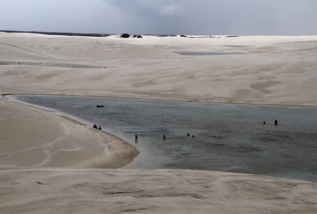 Banhistas na Lagoa Betânia, entre dunas brancas de Santo Amaro do Maranhão, nos Lençóis Maranhenses, sob céu nublado