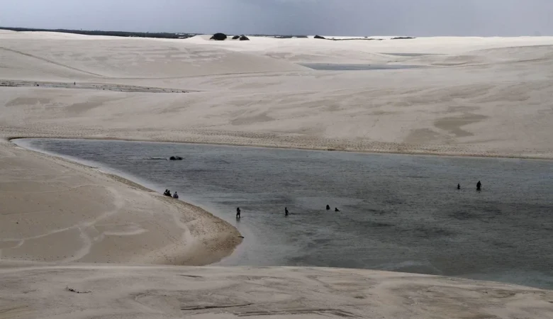 Banhistas na Lagoa Betânia, entre dunas brancas de Santo Amaro do Maranhão, nos Lençóis Maranhenses, sob céu nublado