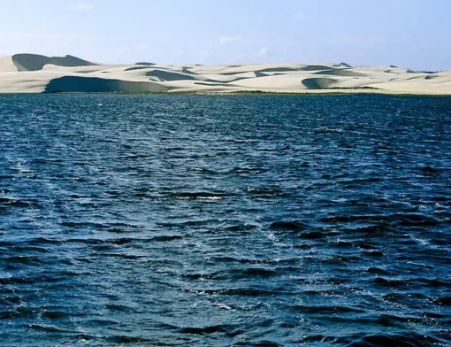 Lagoa do Portinho de água azul escura, com dunas de areia branca ao fundo, no litoral do Piauí