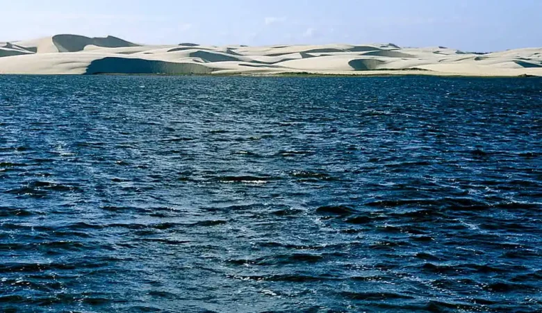 Lagoa do Portinho de água azul escura, com dunas de areia branca ao fundo, no litoral do Piauí