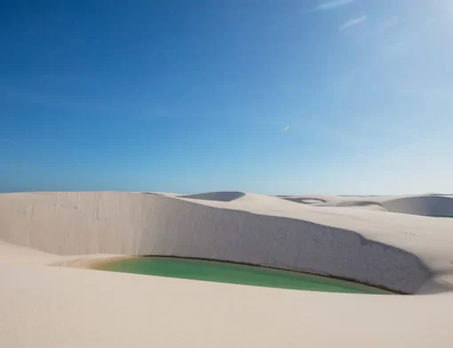 Lagoa de água verde encaixada entre dunas de areia branca, sob céu azul limpo