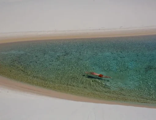 Pessoa nadando em lagoa de água cristalina entre dunas brancas