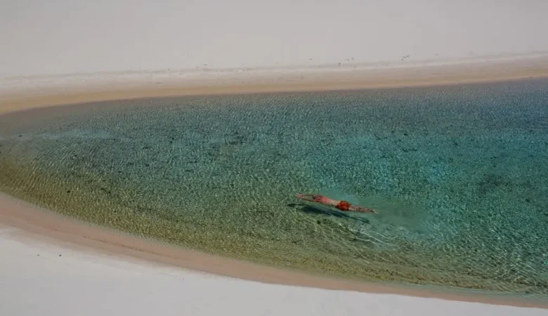 Pessoa nadando em lagoa de água cristalina entre dunas brancas