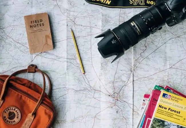Mesa de planejamento de viagem com mapa, câmera fotográfica e roteiro de destinos turísticos