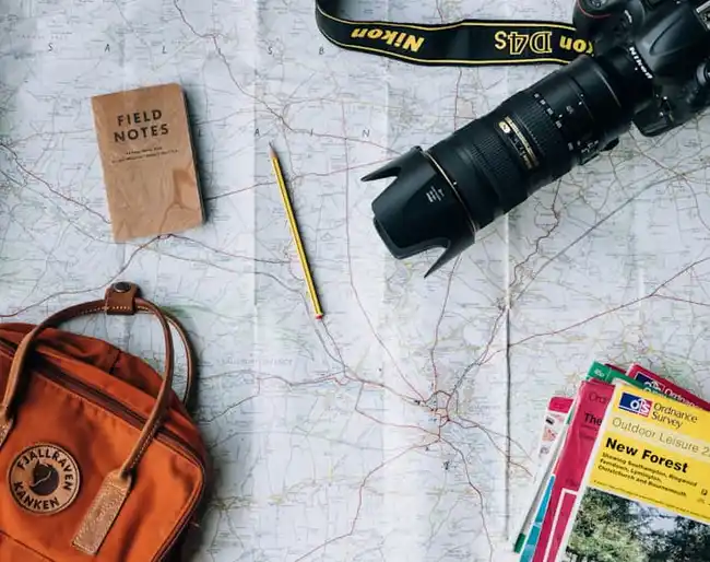 Mesa de planejamento de viagem com mapa, câmera fotográfica e roteiro de destinos turísticos