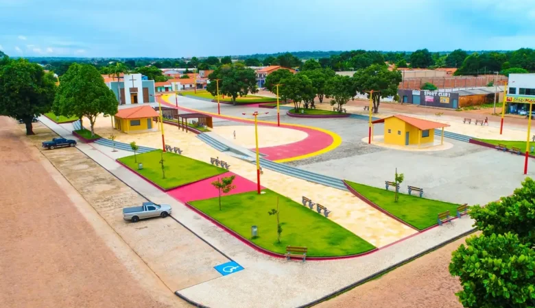 Vista do alto da praça central de Baixa Grande do Ribeiro, com canteiros de grama, piso colorido, quiosques amarelos e a igreja ao fundo