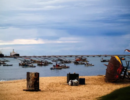 Jangadas e barcos de pesca ancorados na enseada do Mucuripe, em Fortaleza, com o píer do porto e navios ao fundo