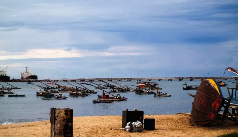 Jangadas e barcos de pesca ancorados na enseada do Mucuripe, em Fortaleza, com o píer do porto e navios ao fundo