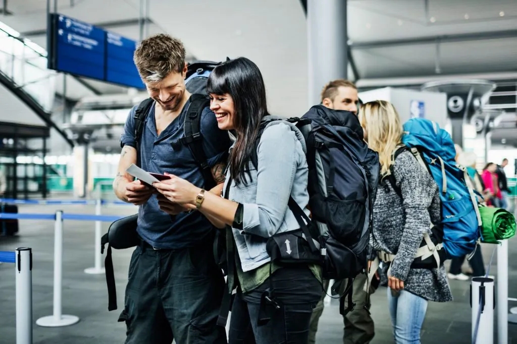 Casal de viajantes com mochilas sorrindo ao conferir os cartões de embarque no aeroporto